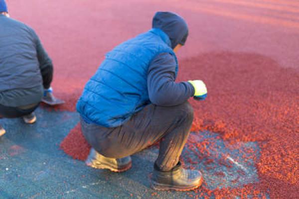 A man in winter clothes works to put rubber mulch on a playground surface